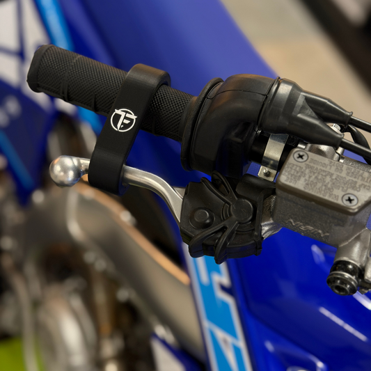 Close-up of motorcycle handlebar with throttle grip and brake lever on a blue background with TVE Brake Depresser